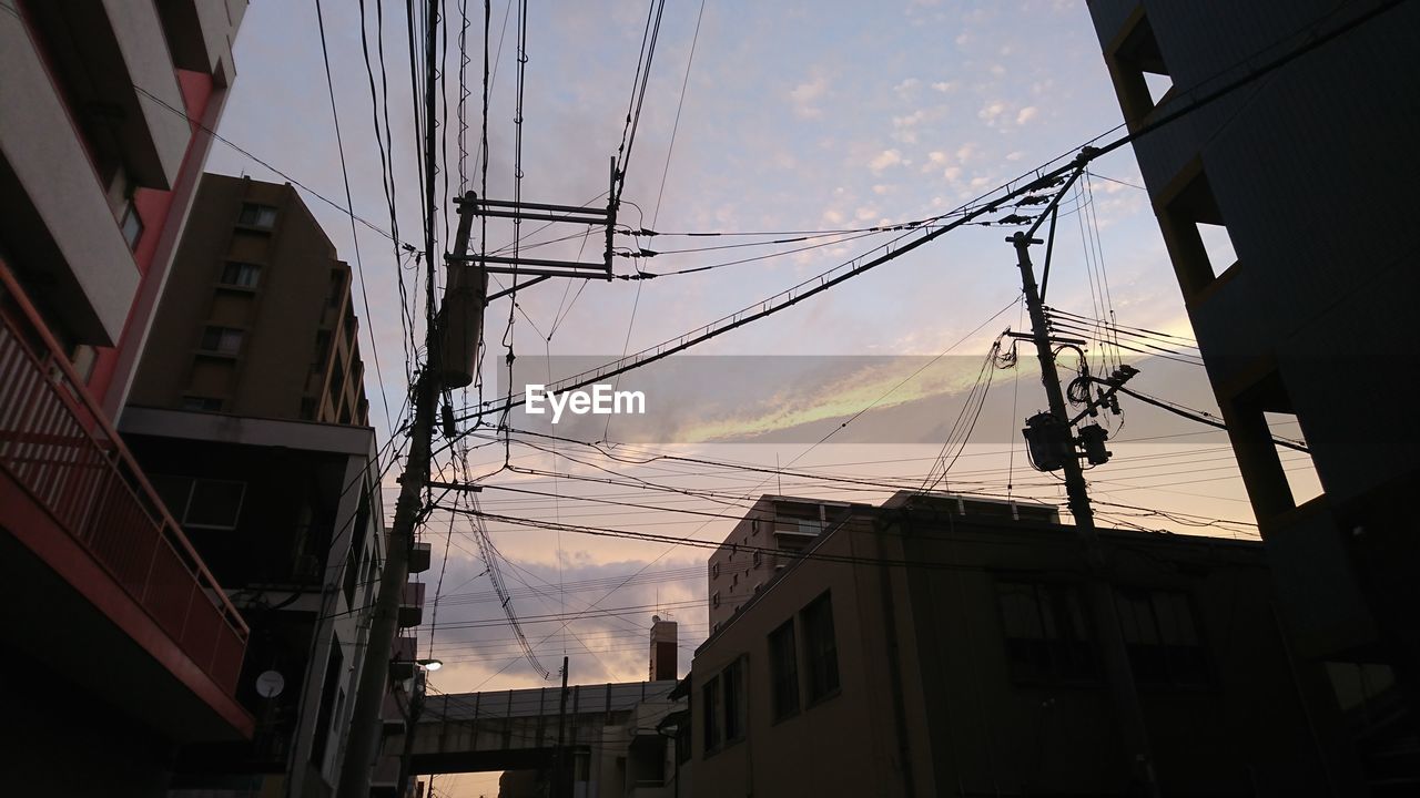 Low angle view of electricity pylon and buildings against sky during sunset