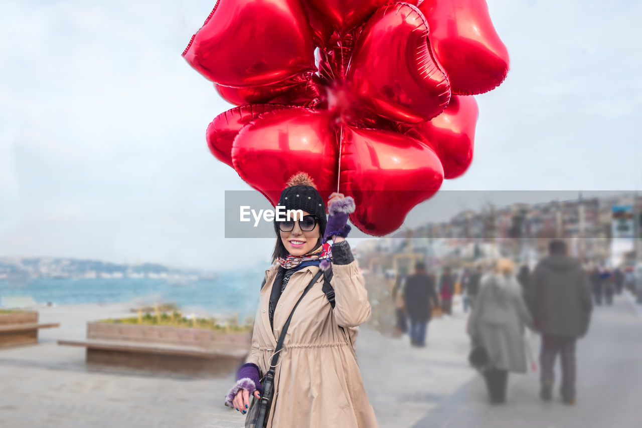 Portrait of woman with red balloons standing on street
