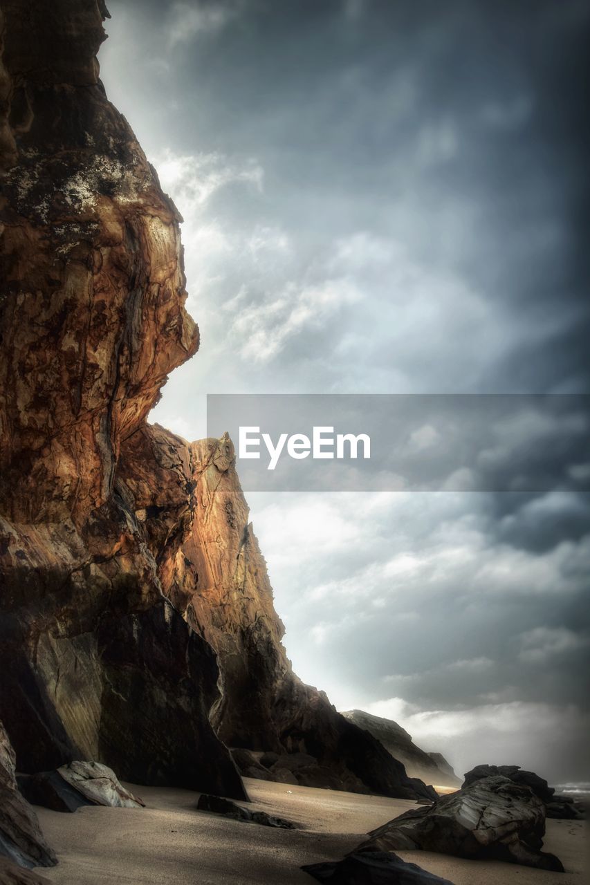 Low angle view of rock formation on shore against cloudy sky