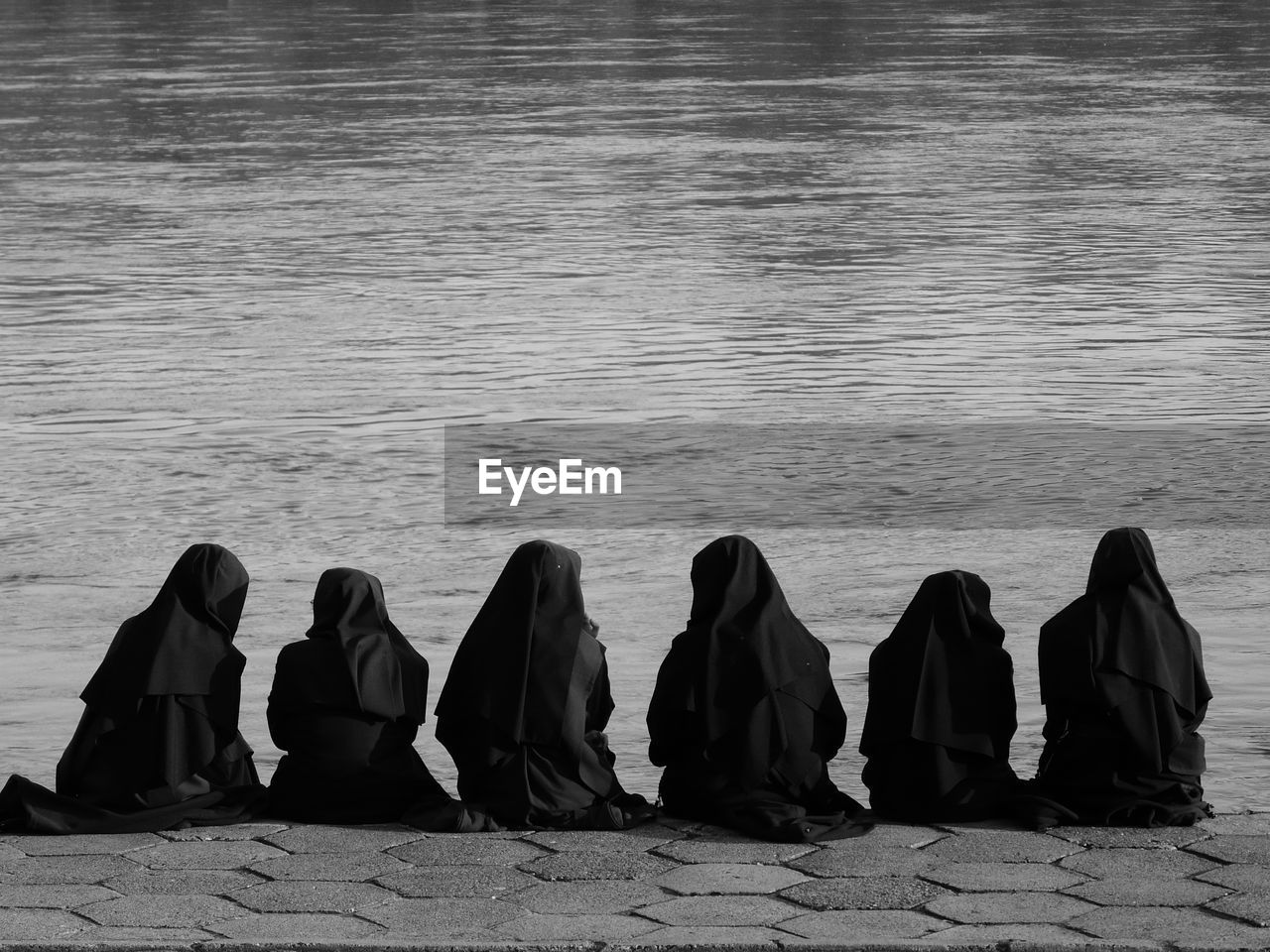 Rear view of women hijab praying at lakeshore