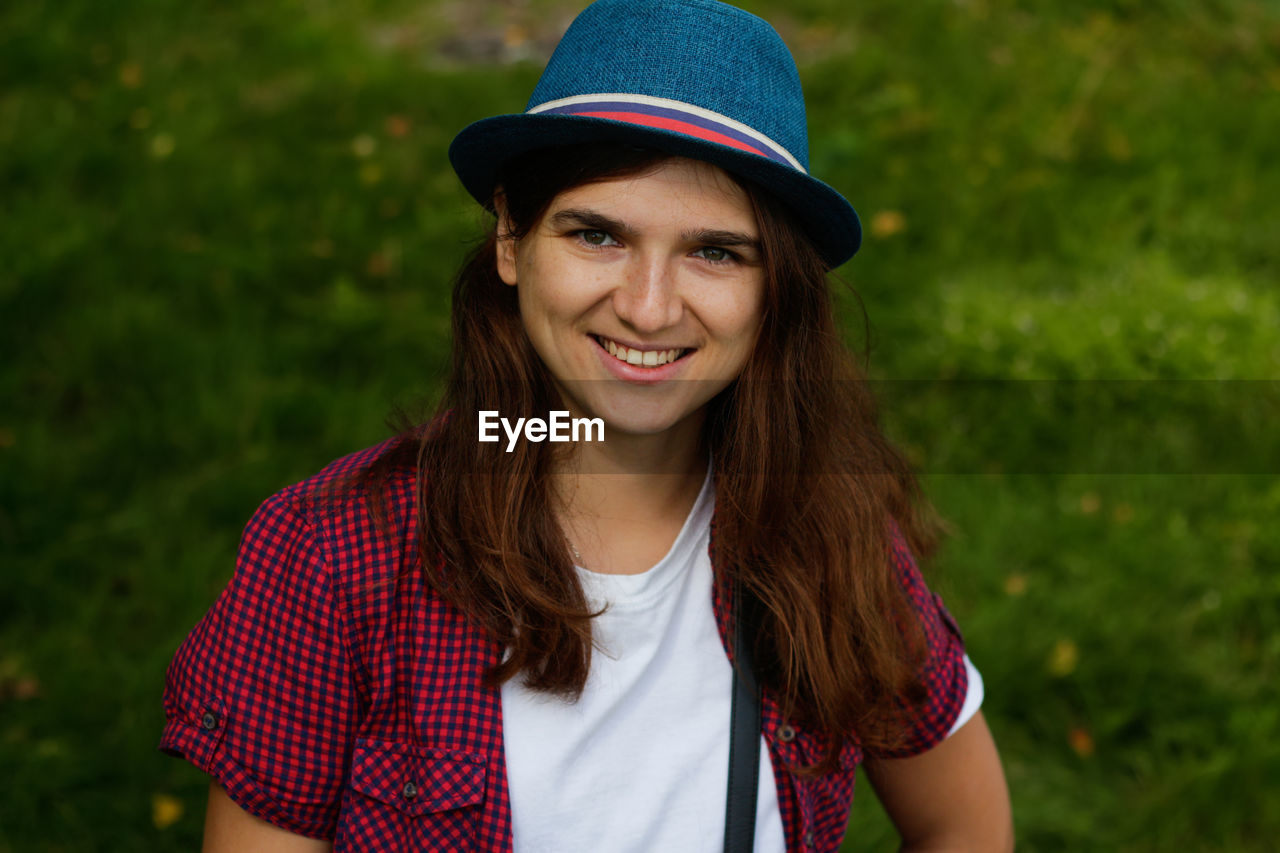 Portrait of a beautiful smiling young woman with brown hair wearing a hat and looking at camera 