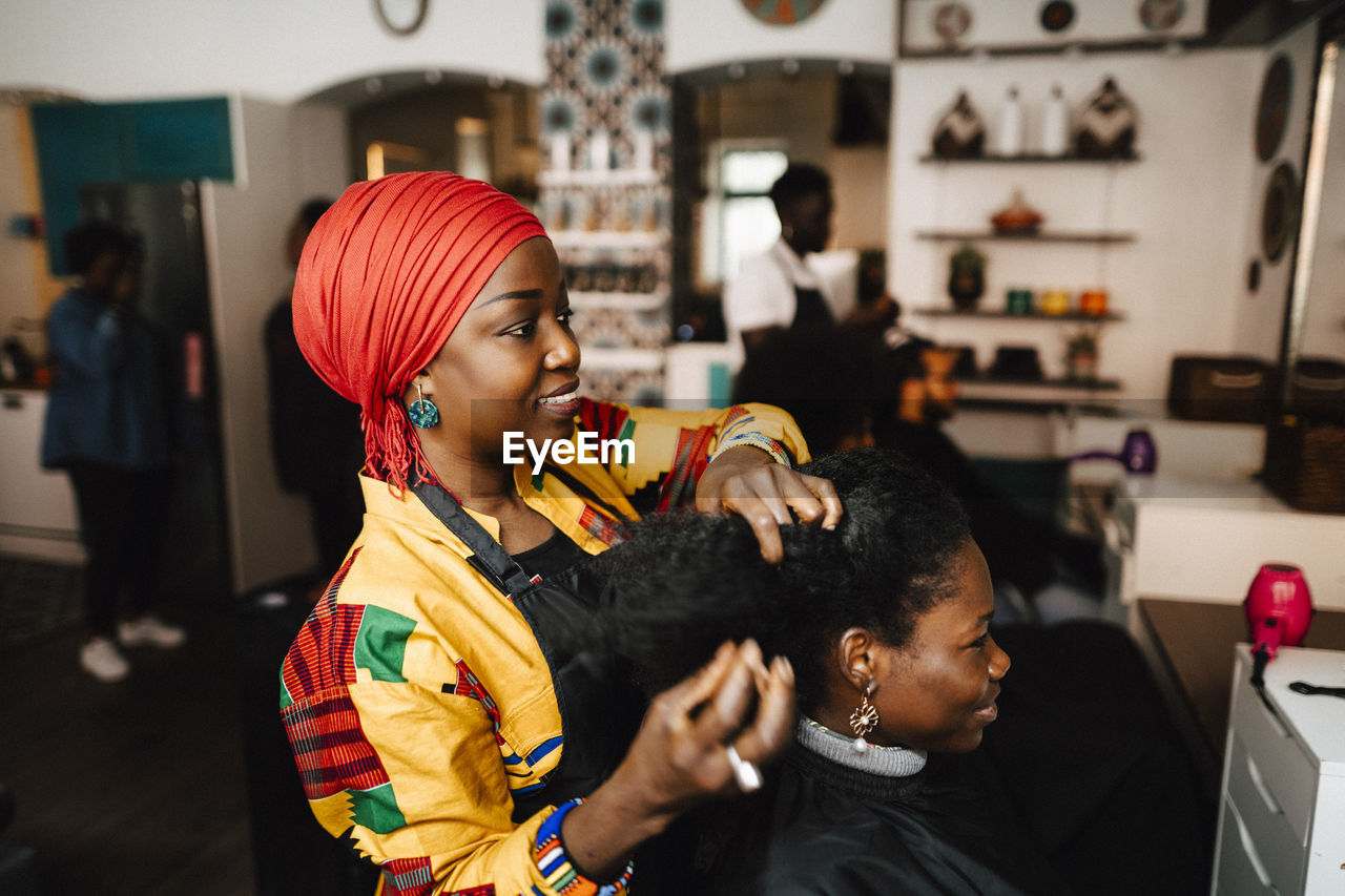 Female barber making hairstyle of customer in hair salon