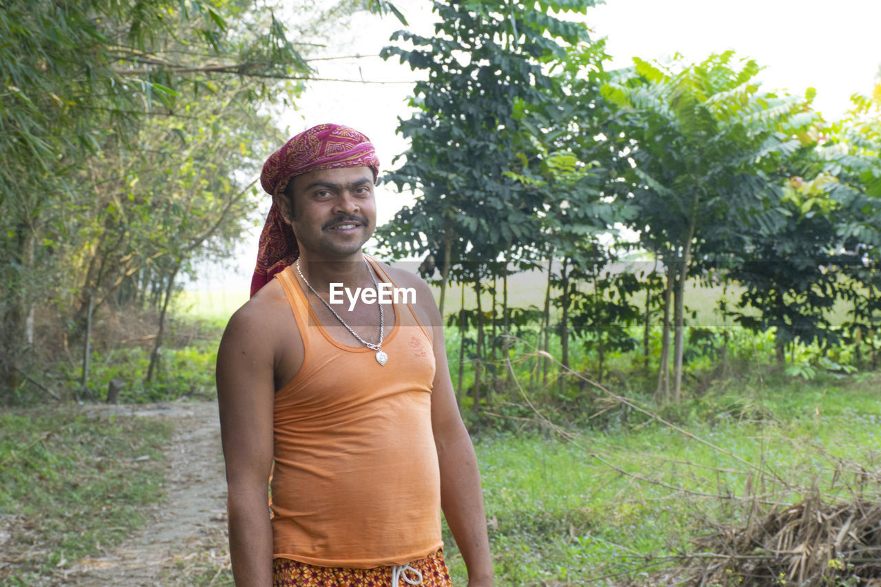 Portrait of young farmer standing against trees