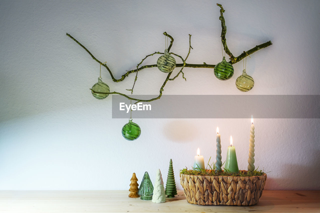 candle, green, nature, plant, indoors, branch, fire, burning, no people, decoration, flame, celebration, tree, table, lighting, food, illuminated, food and drink, environment, wall - building feature, still life