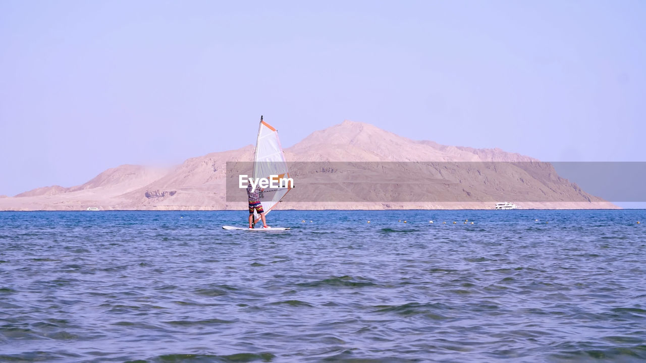 Man learns to ride on a board with a sail, windsurfing. windsurfing on the crystal clear water. 