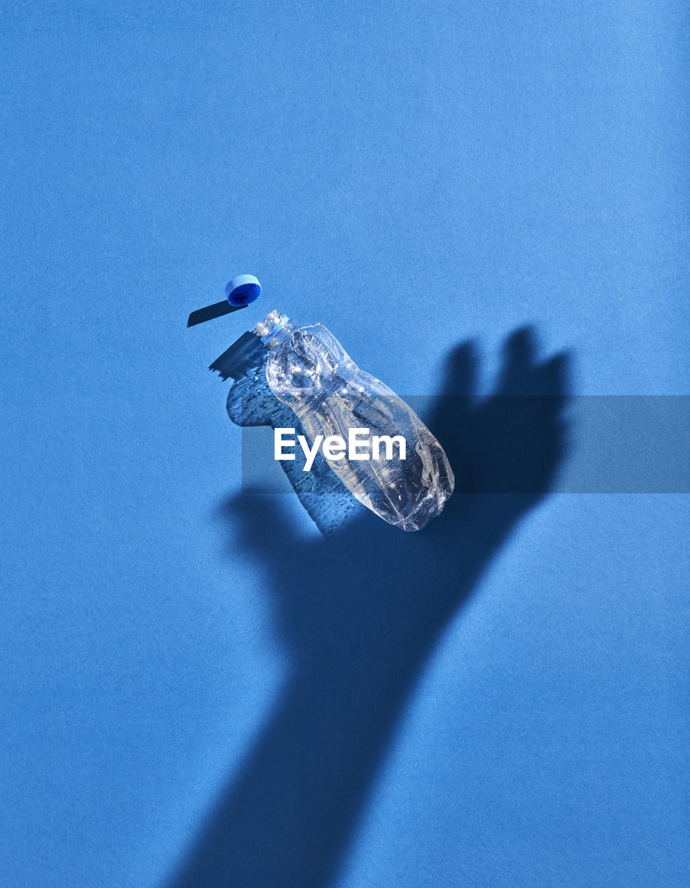 Shadow of a hand and plastic bottle, blue background
