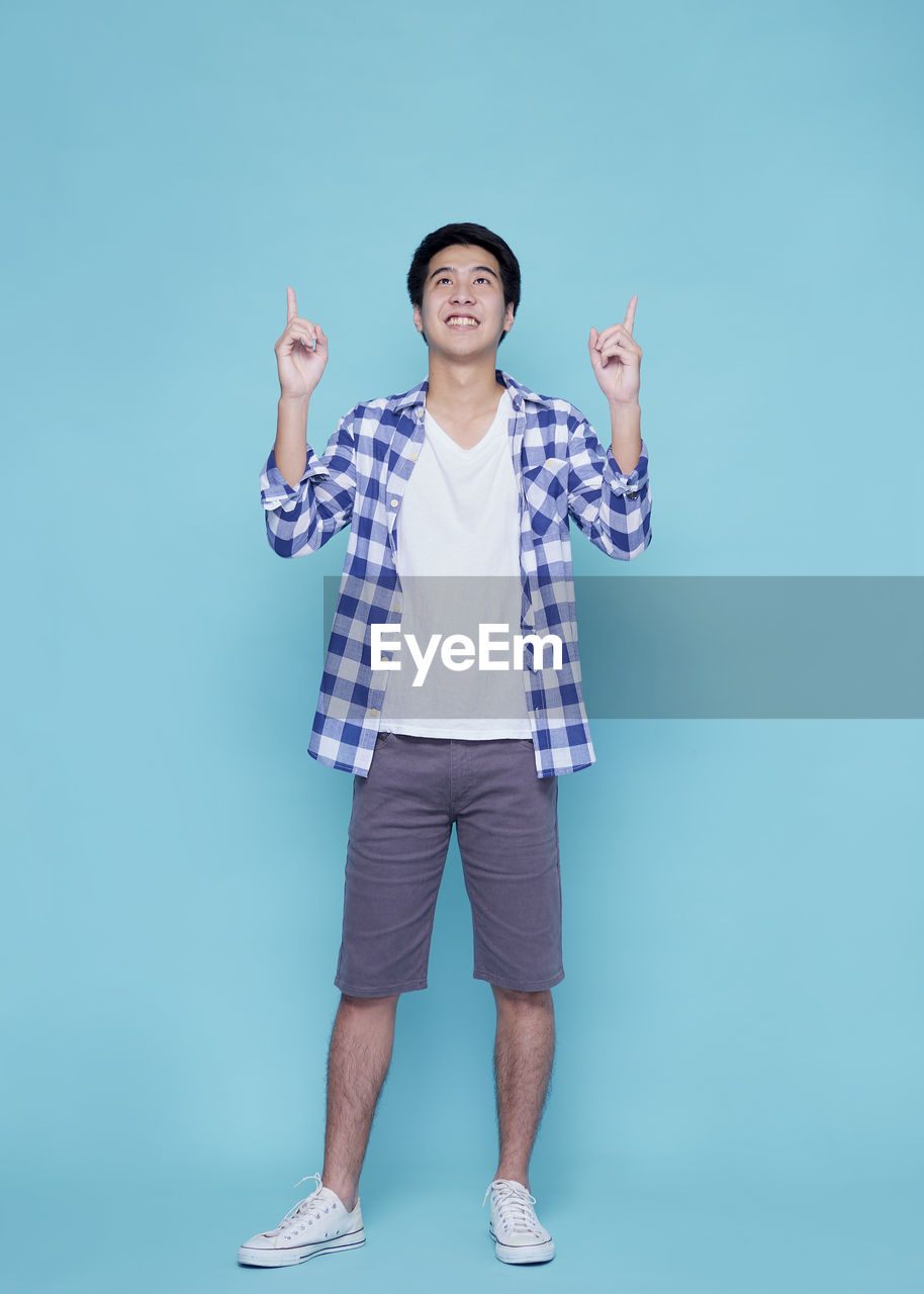 PORTRAIT OF SMILING YOUNG MAN AGAINST BLUE BACKGROUND