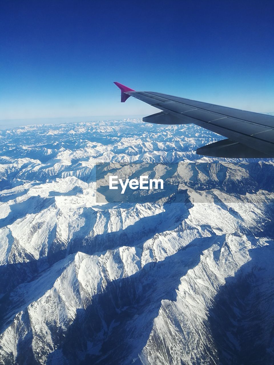 AERIAL VIEW OF AIRPLANE WING OVER LANDSCAPE AGAINST BLUE SKY