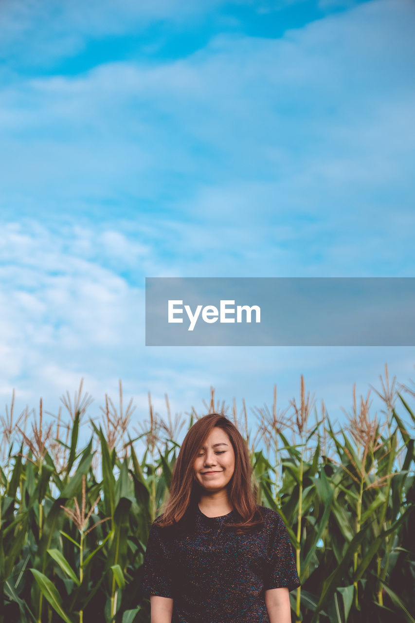 Smiling beautiful woman with eyes closed standing at farm against sky