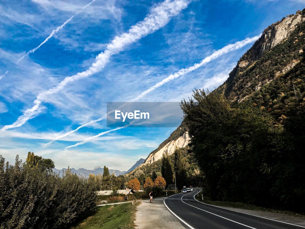 Road by trees against blue sky