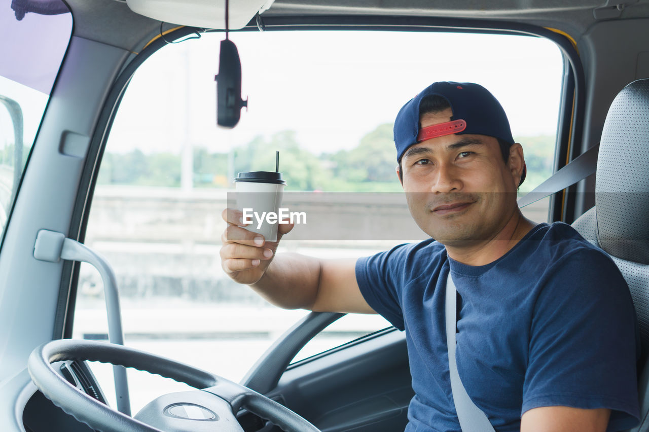 Portrait of man holding coffee while sitting in truck
