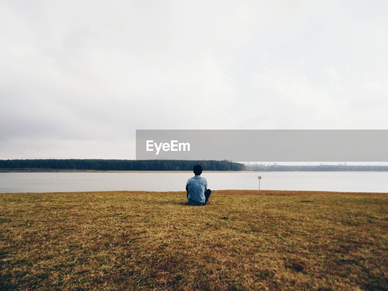 Rear view of man sitting at riverbank against sky