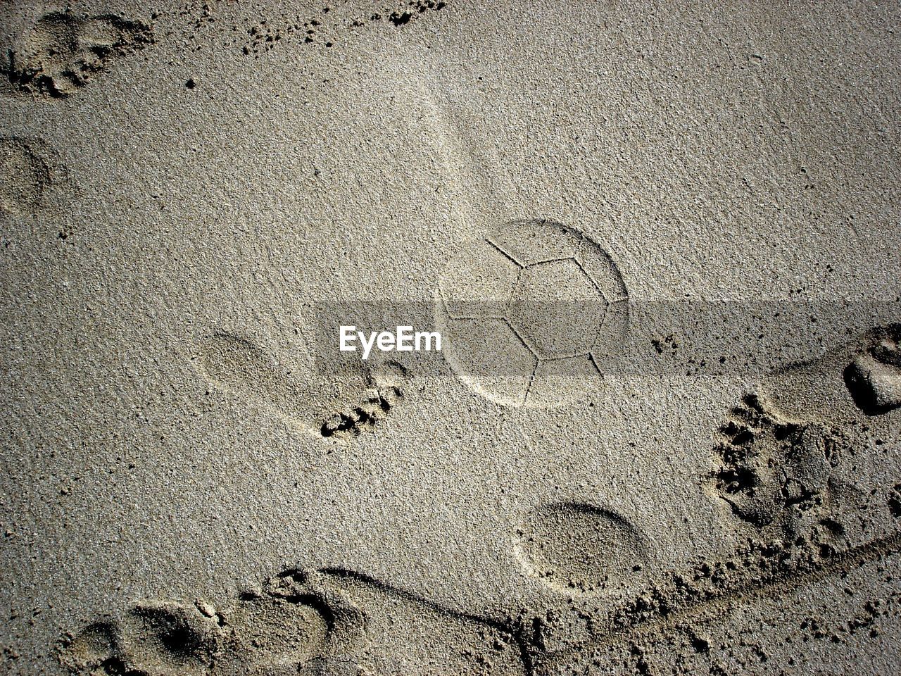 Close-up of foot and soccer ball imprints on beach sand