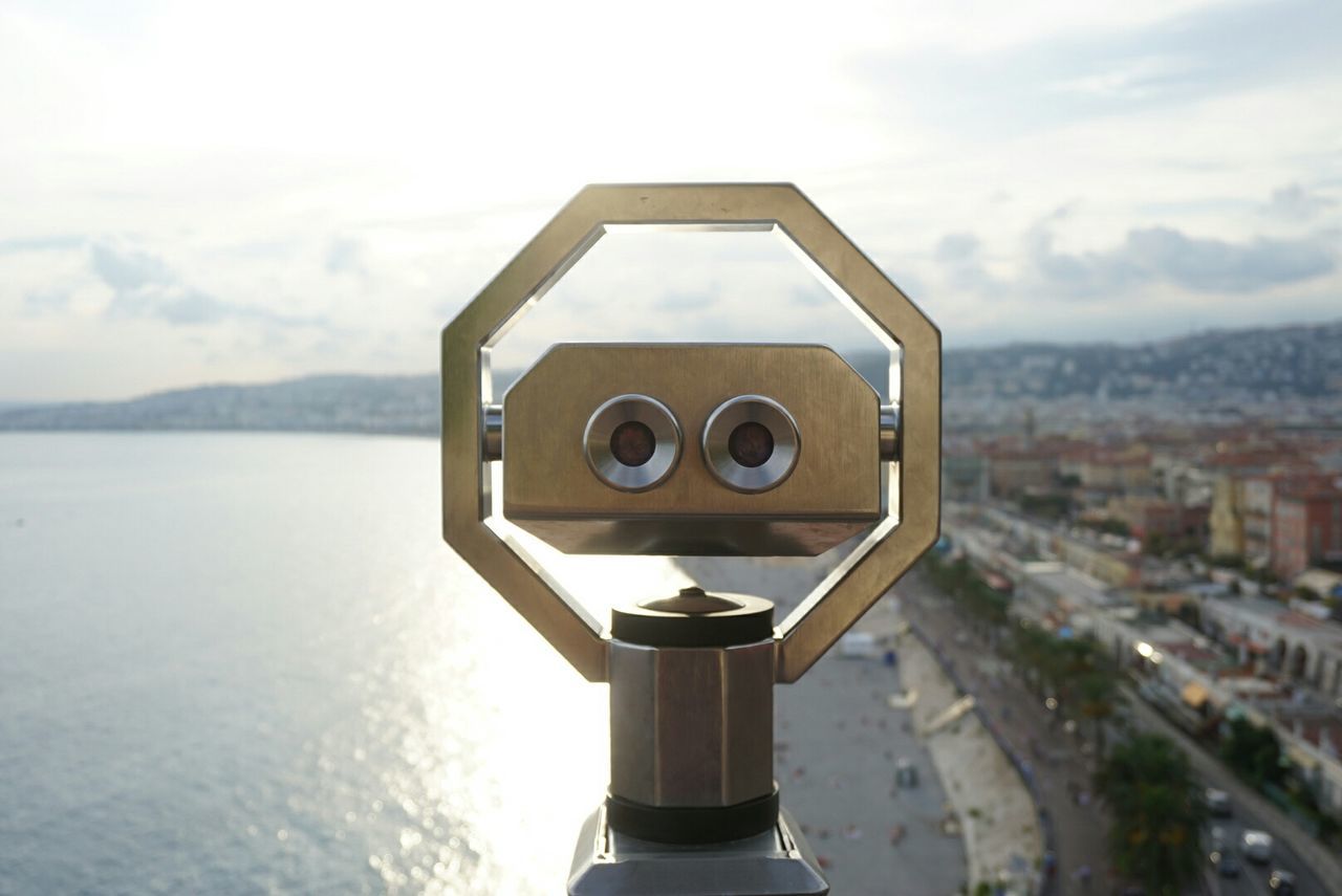 Sea in front of coin-operated binocular against sky