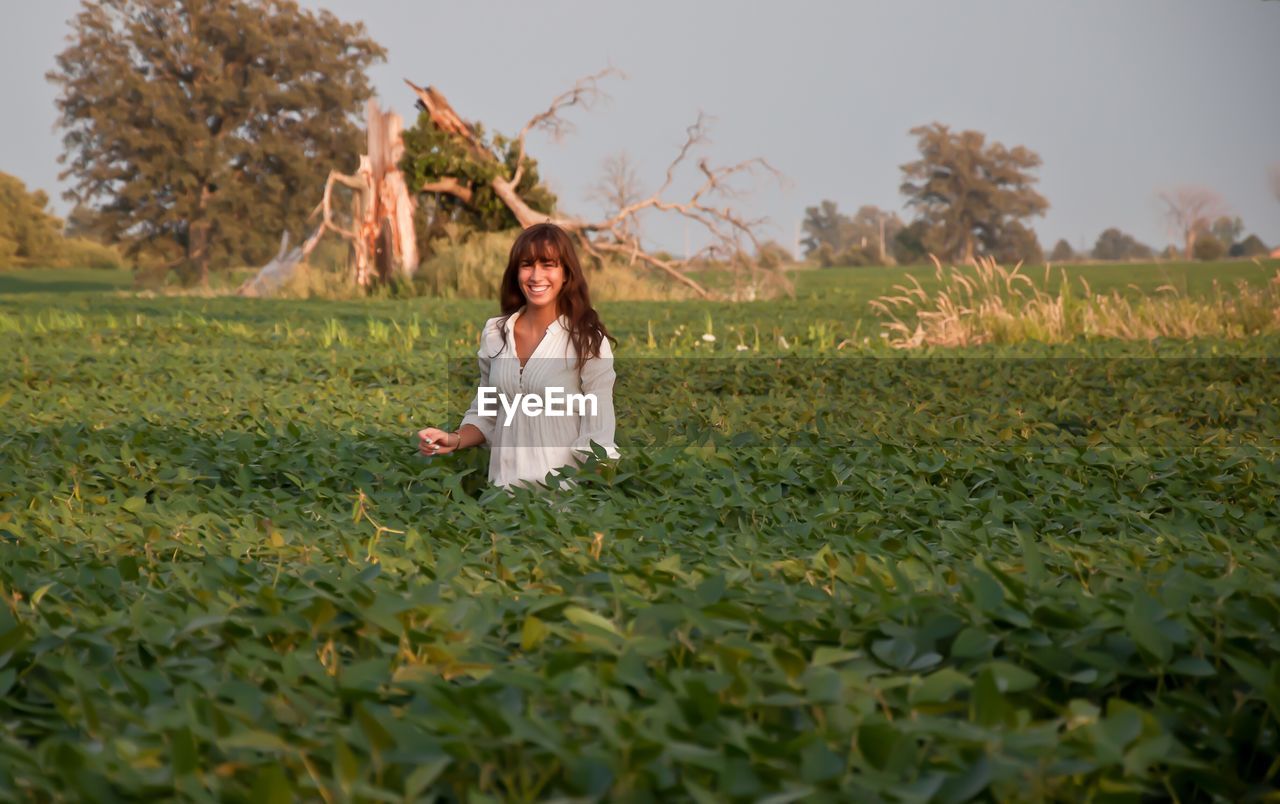 YOUNG WOMAN ON FIELD AGAINST TREES