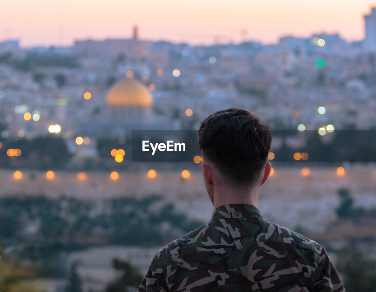 Rear view of man against cityscape during sunset