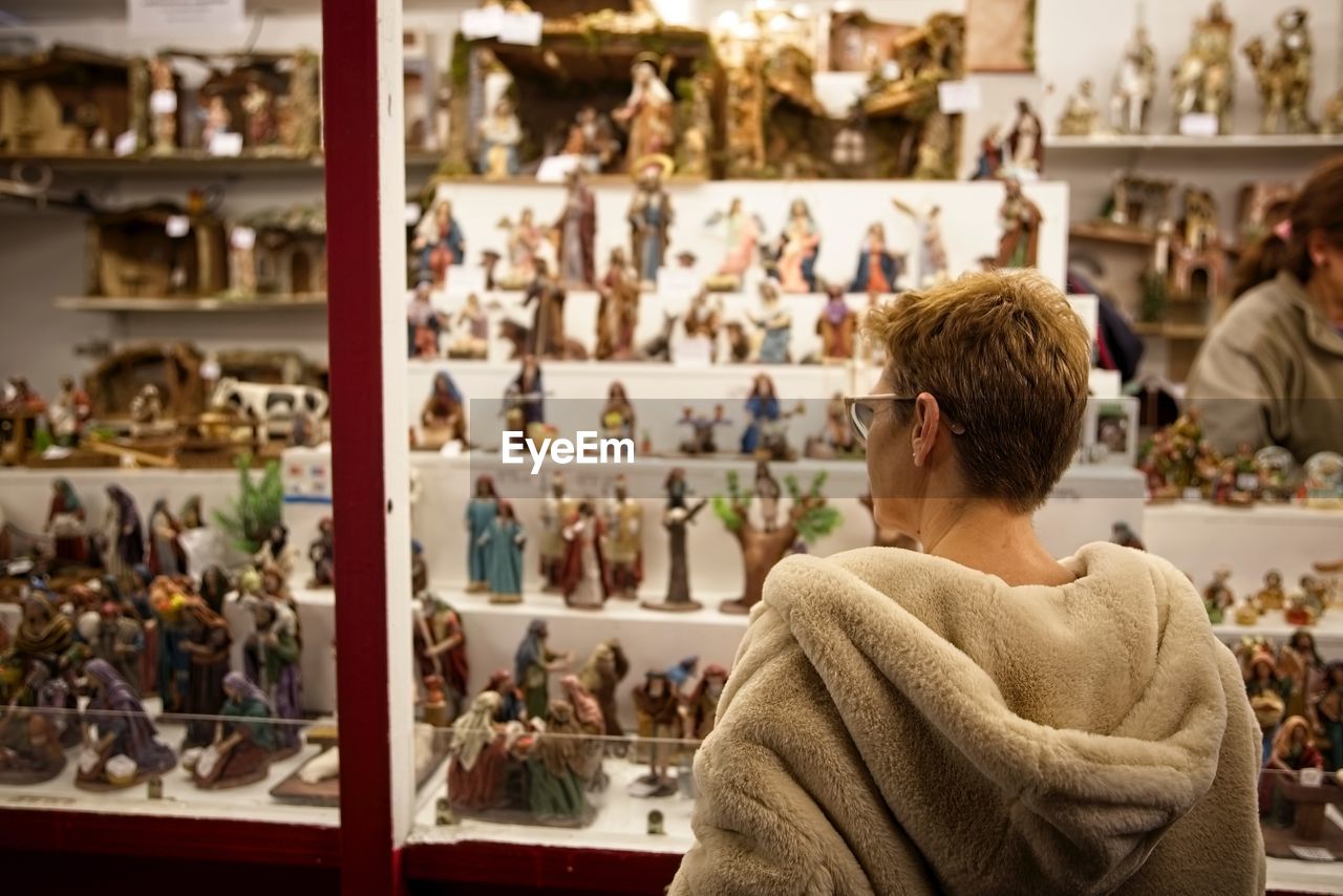 Rear view of woman buying figurines at market during night