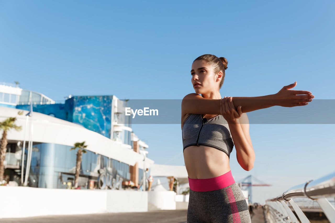 Low angle view of woman exercising against clear blue sky