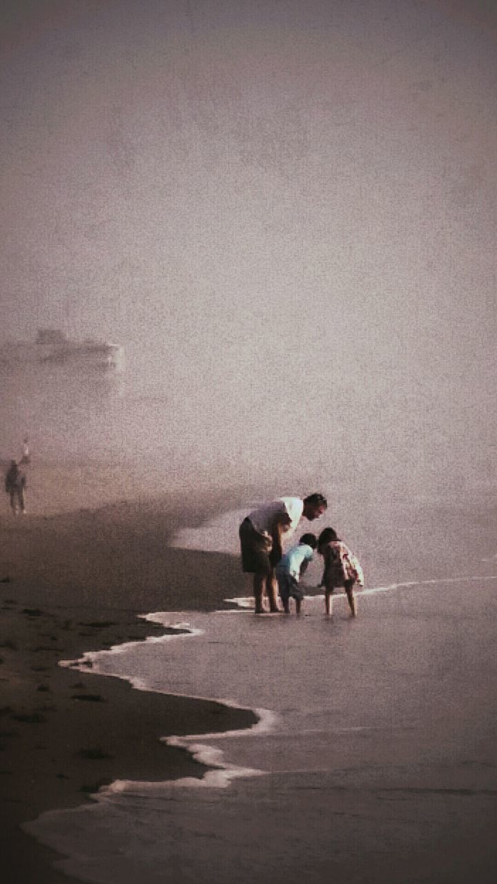 Father with children on beach against sky