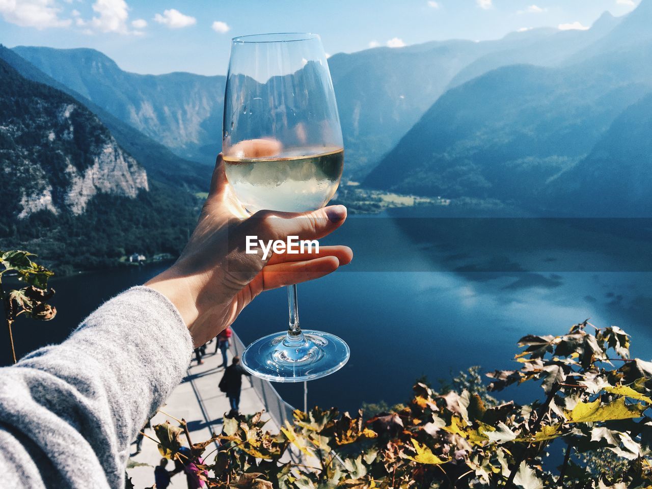 Close-up of human hand holding alcoholic drink by lake against mountains