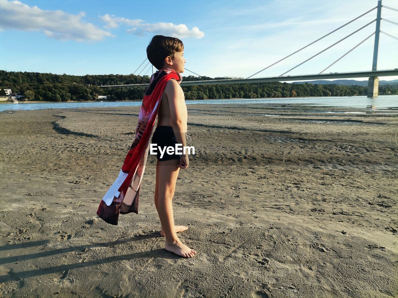 Full length of superhero boy standing on the beach at sunset. 