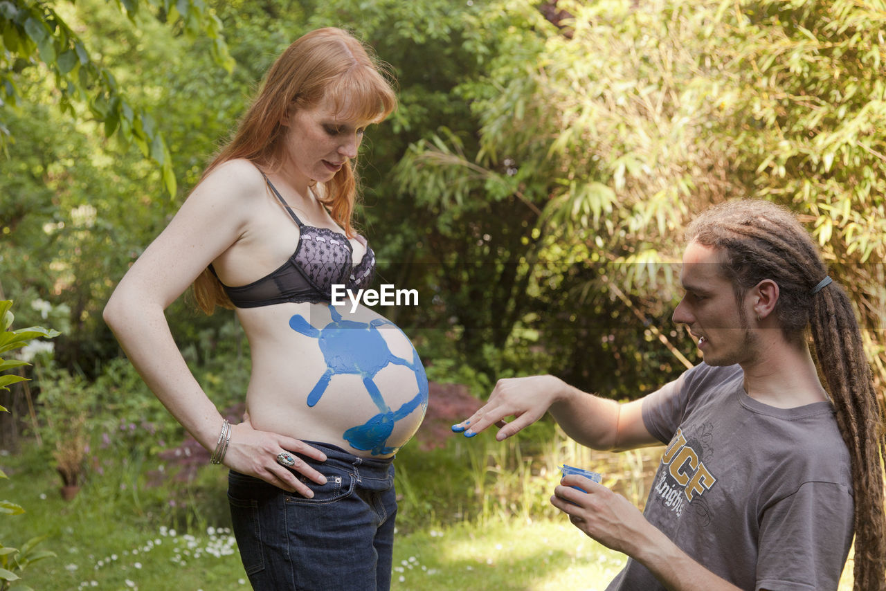 Man finger painting soccer ball on woman's pregnant stomach