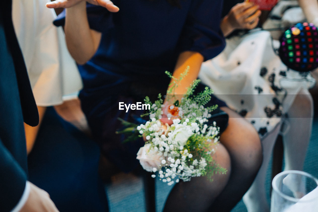 MIDSECTION OF MAN HOLDING BOUQUET IN FRONT OF FLOWERS