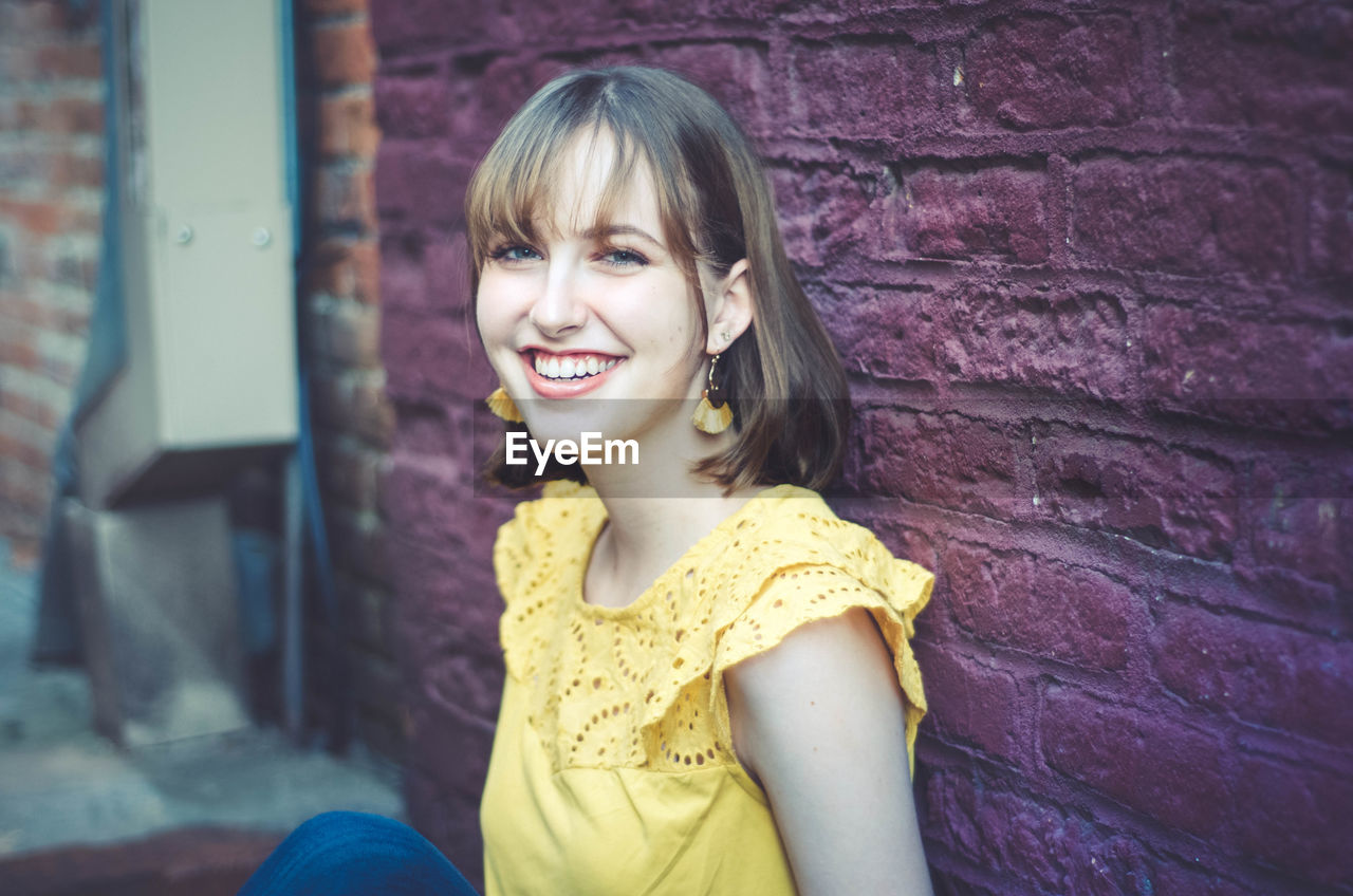 Portrait of smiling young woman against wall