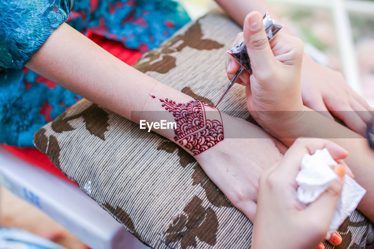 Cropped image of beautician making henna tattoo on woman hand