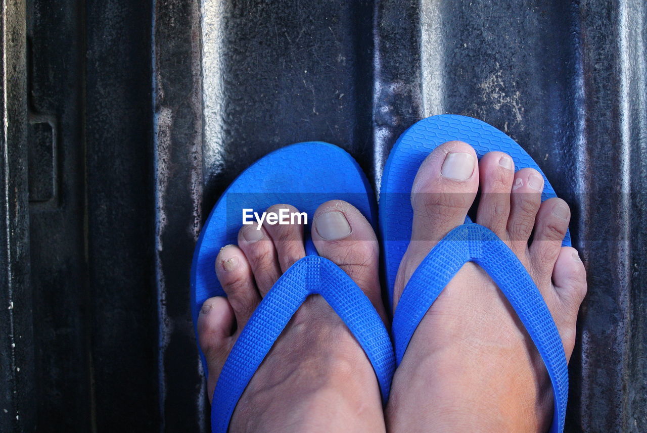 Low section of person wearing blue flip-flop standing on metallic surface