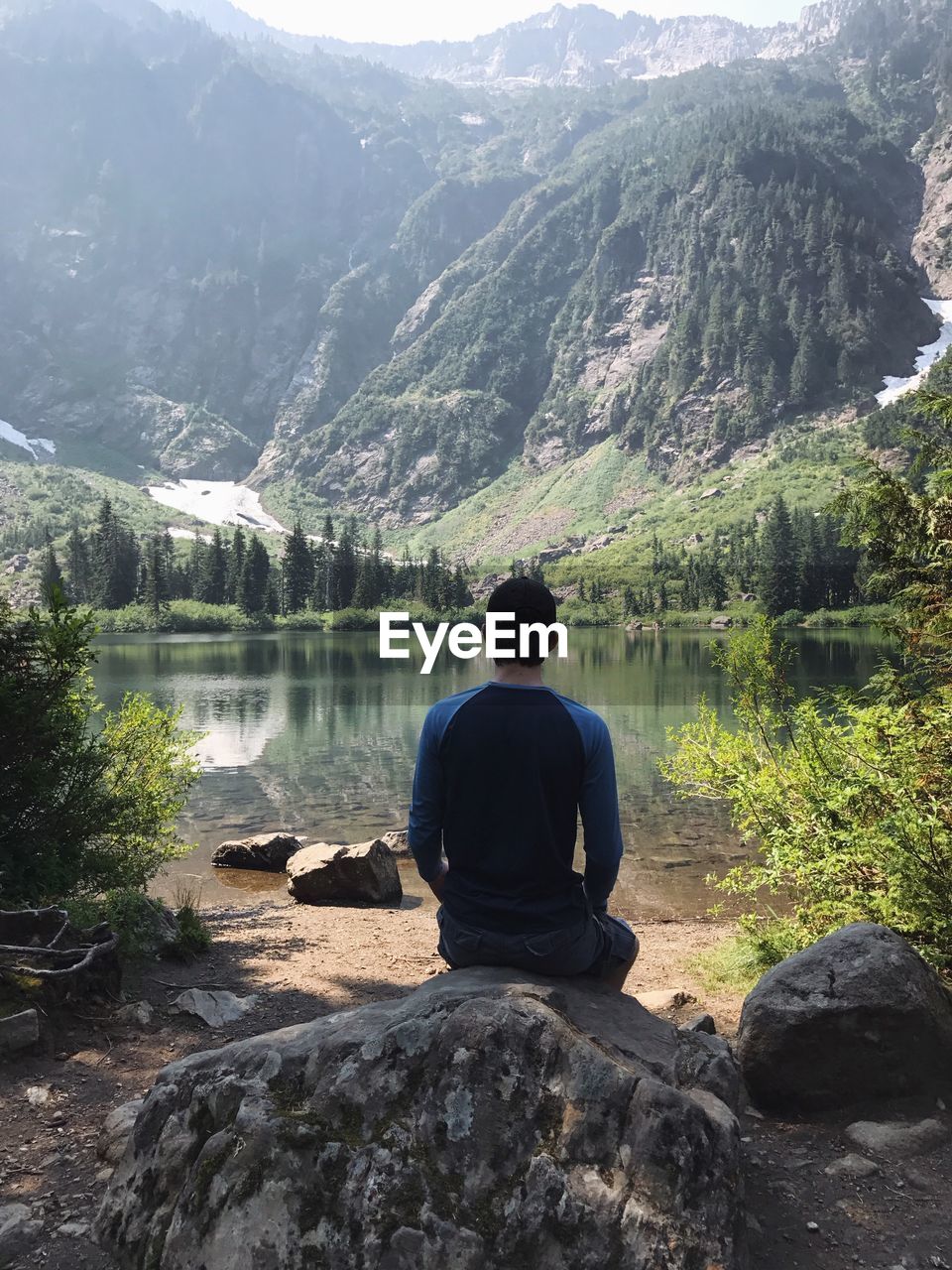 Rear view of man sitting on rock at lake