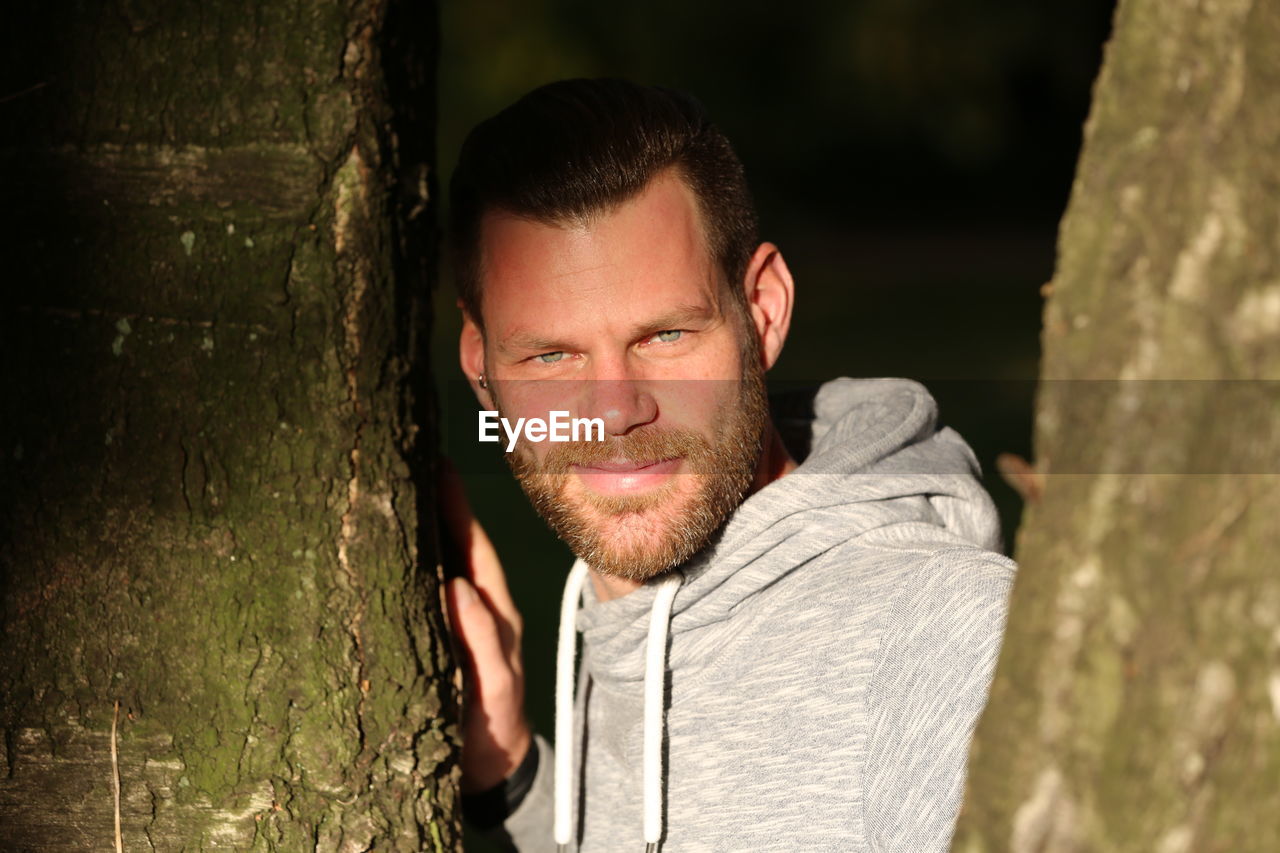 Close-up portrait of man standing by tree trunk