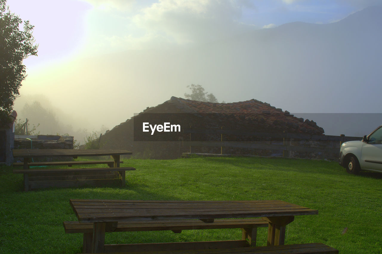 EMPTY BENCH ON FIELD BY MOUNTAINS AGAINST SKY