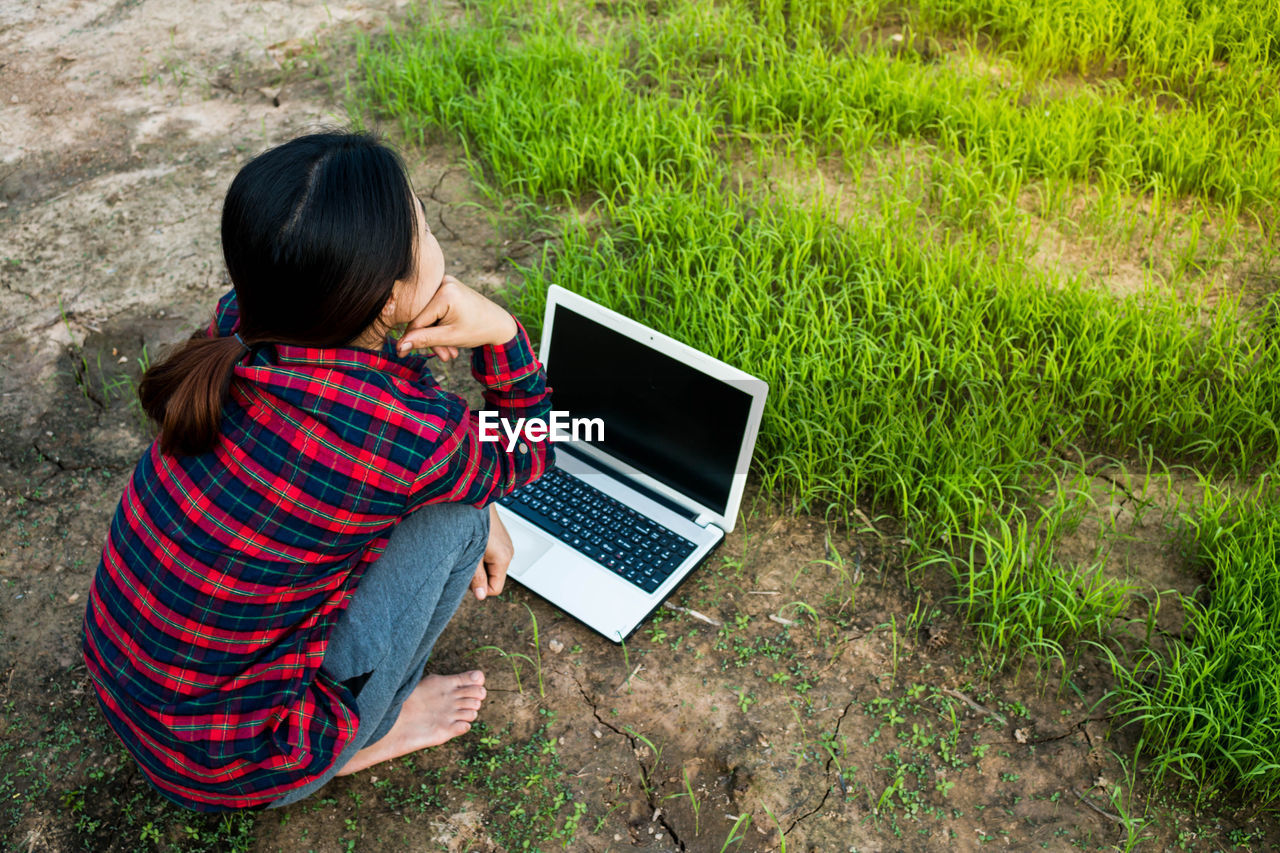 Rear view of woman crouching by laptop on field
