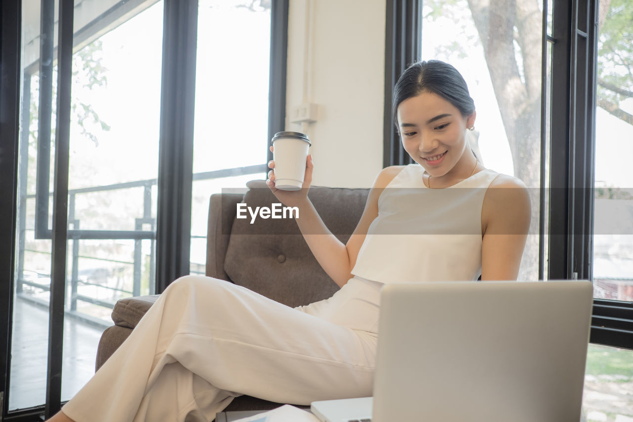 Young woman having coffee while sitting on chair in office