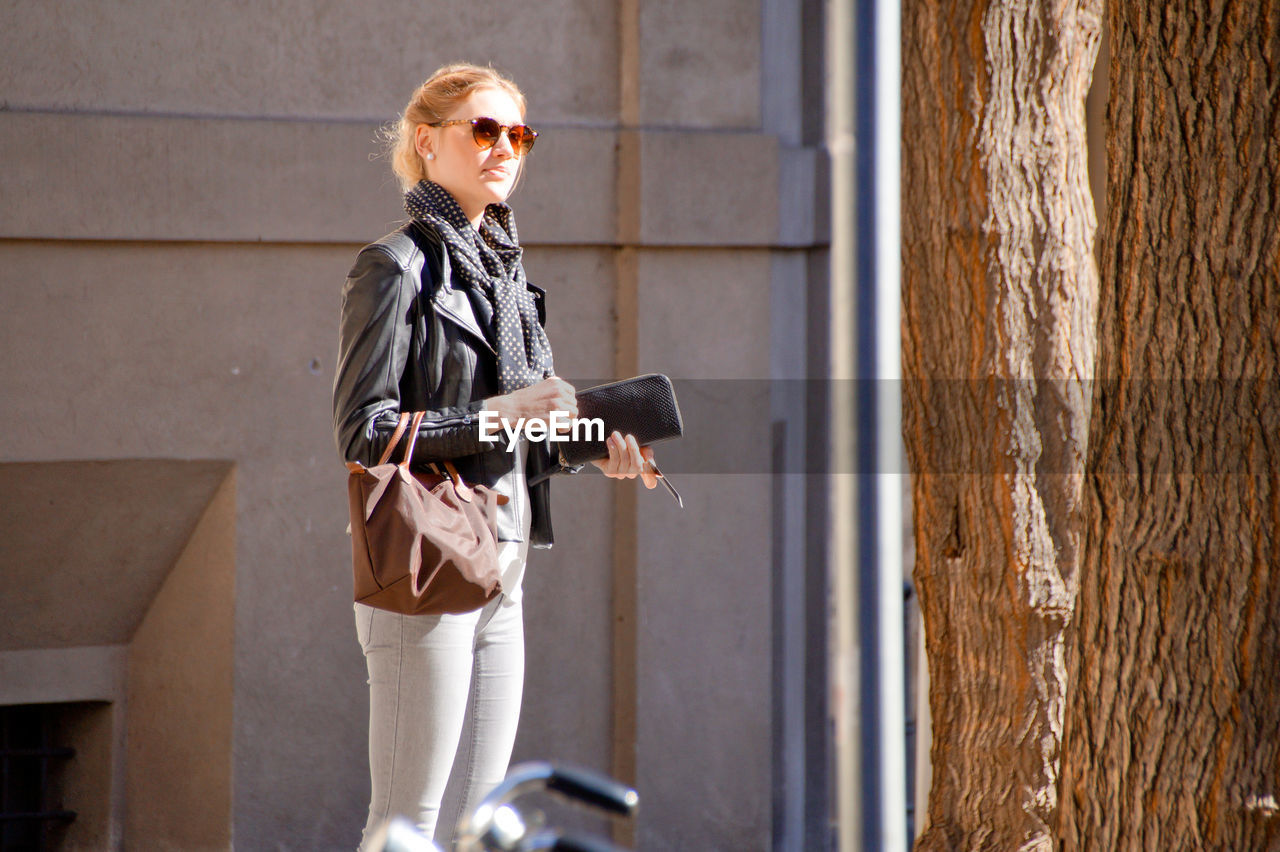 Young woman holding pouch while standing by building