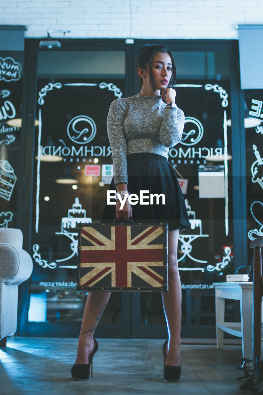 Full length of young woman holding briefcase while standing in store