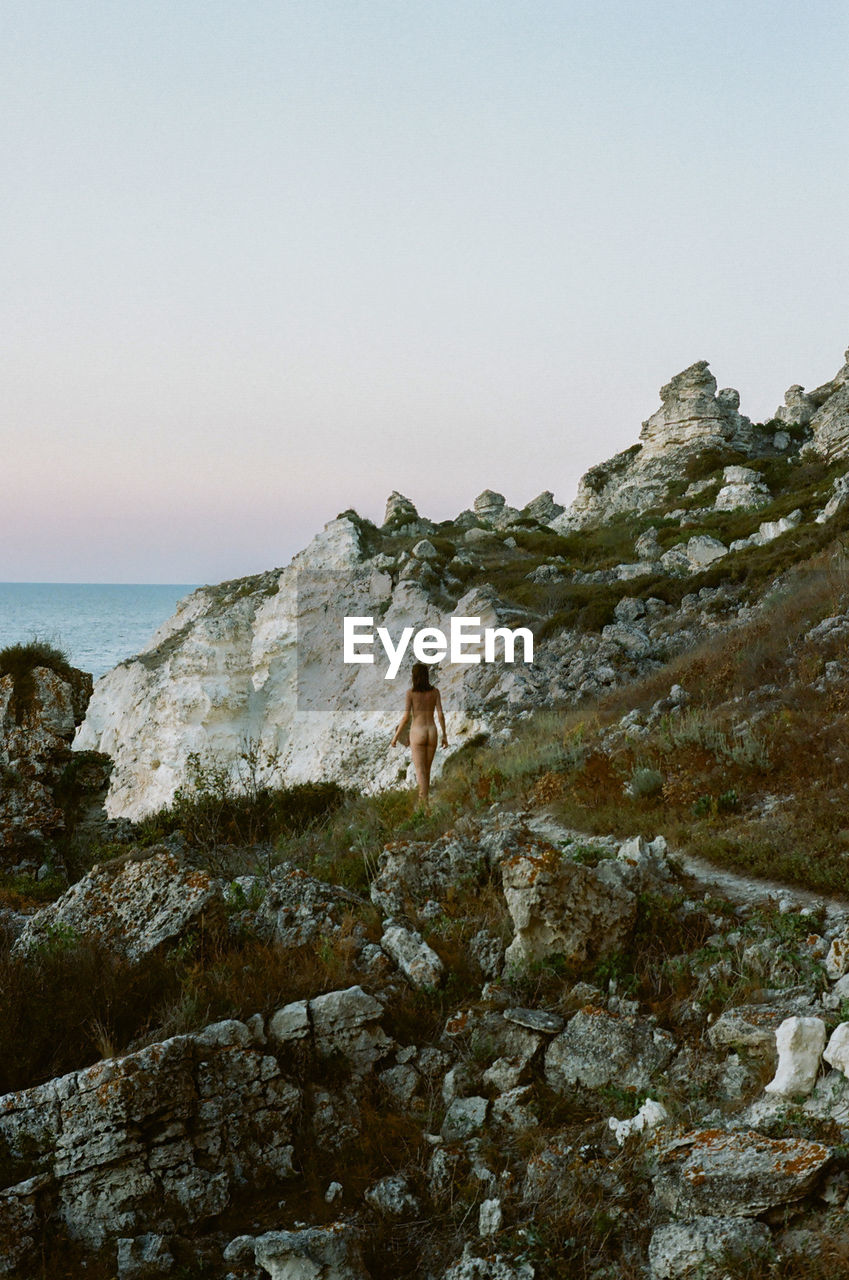 Naked woman walking on rock formation against clear sky