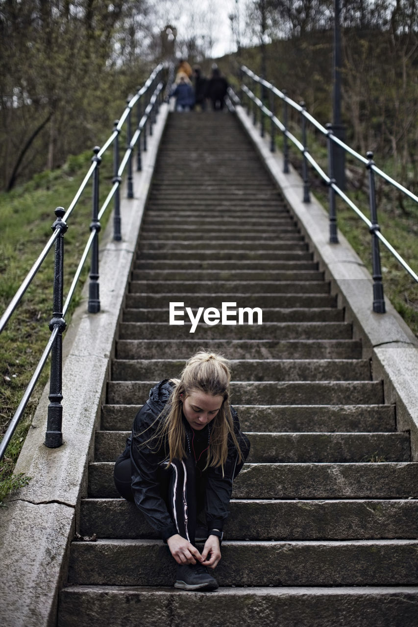 Full length of young woman tying shoelace on steps