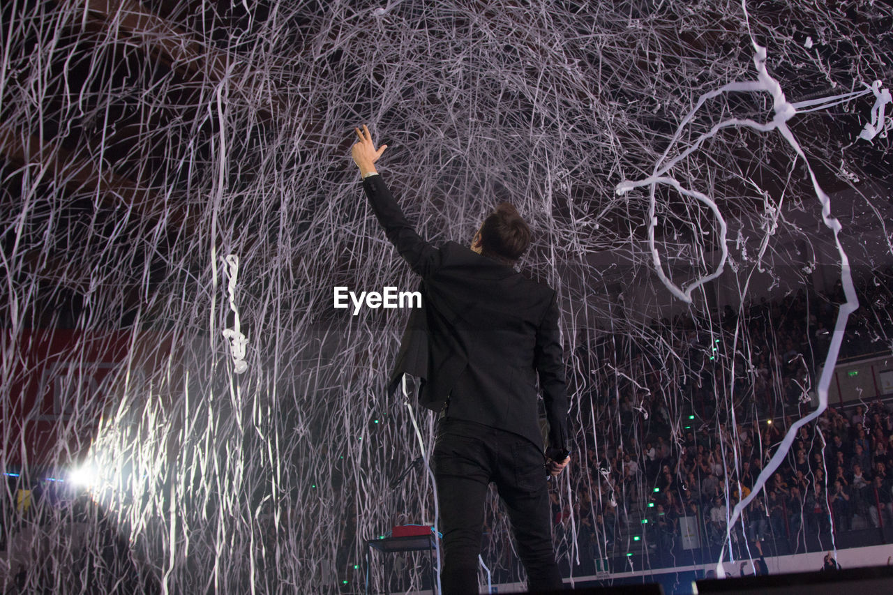 REAR VIEW OF MAN STANDING BY ILLUMINATED PLANTS