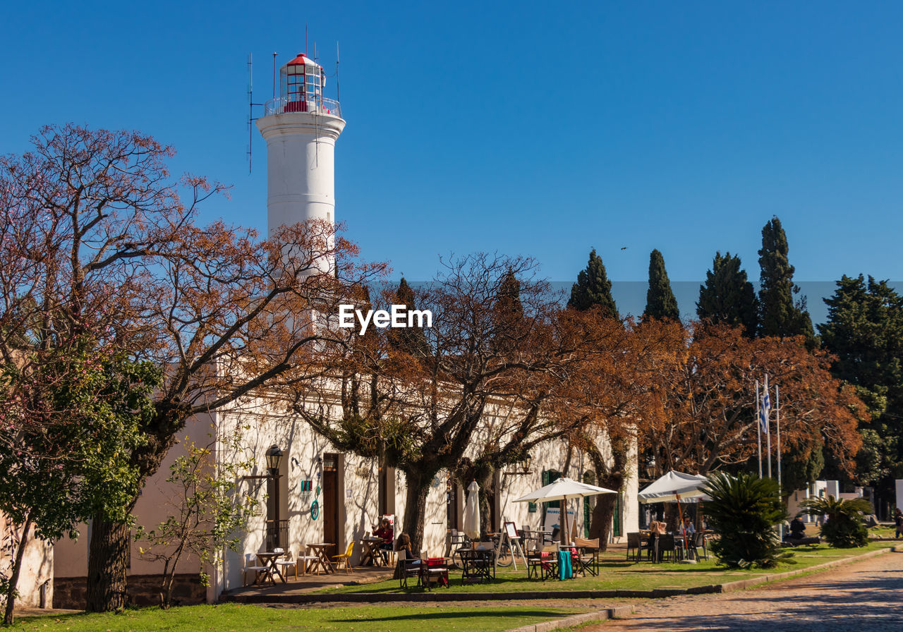 LOW ANGLE VIEW OF LIGHTHOUSE AGAINST TREES AND BUILDINGS