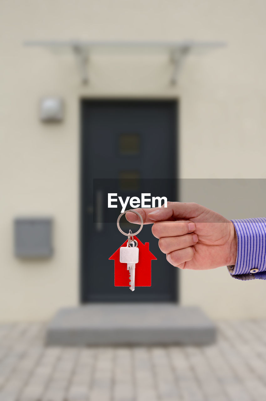 Cropped hand of man holding key ring against house
