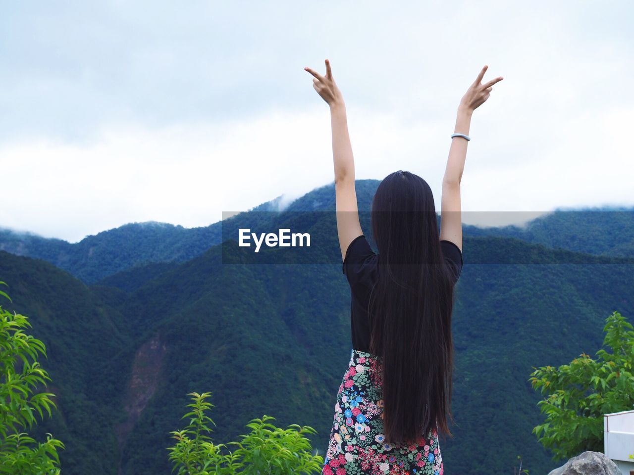 Rear view of woman gesturing peace sign against mountains