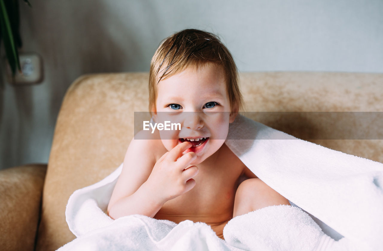 Cute baby in a big white towel. holds fingers in the mouth.