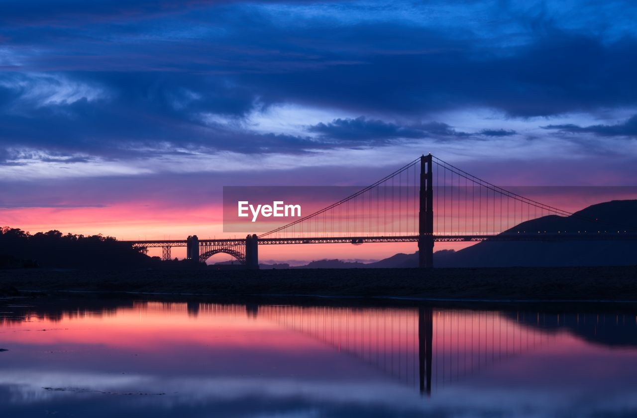 Silhouette of suspension bridge against cloudy sky