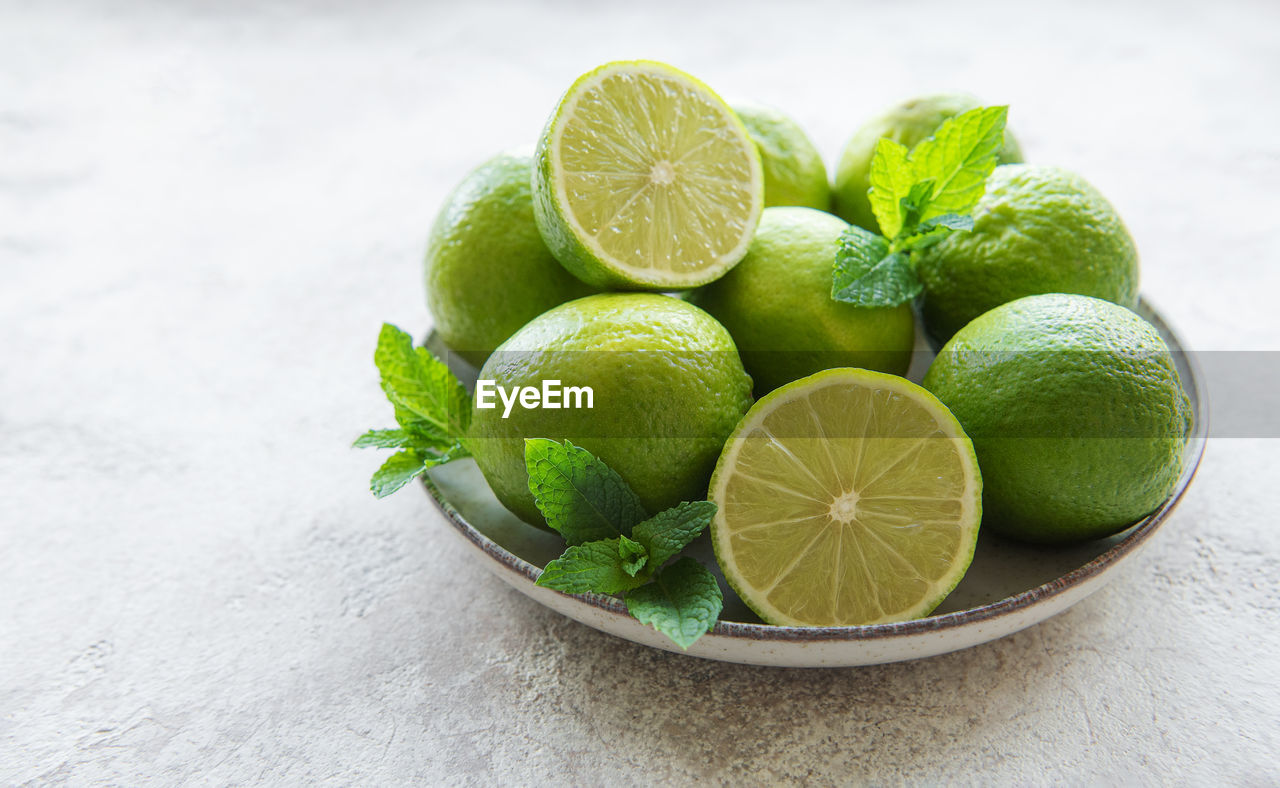 Green limes with fresh mint leaves on plate, concrete background