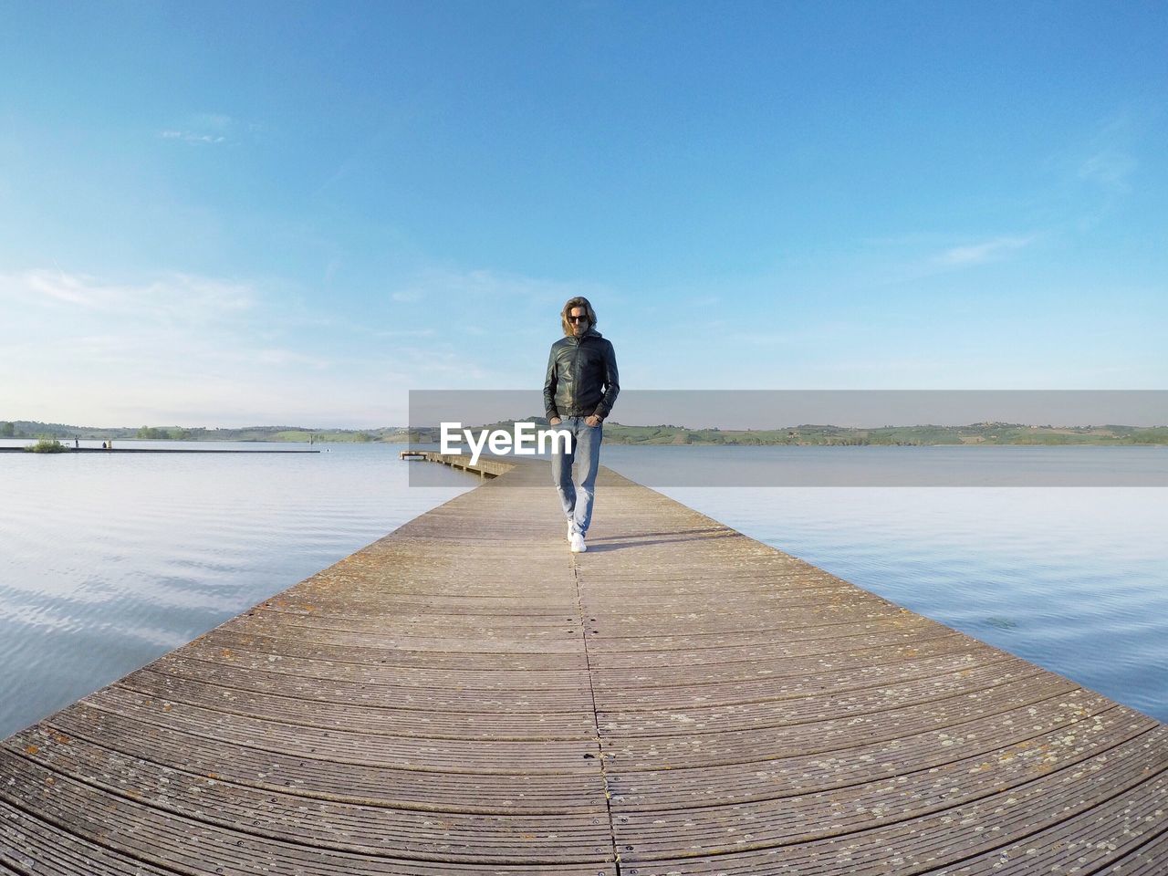 Fish-eye view of man walking on jetty over lake against blue sky