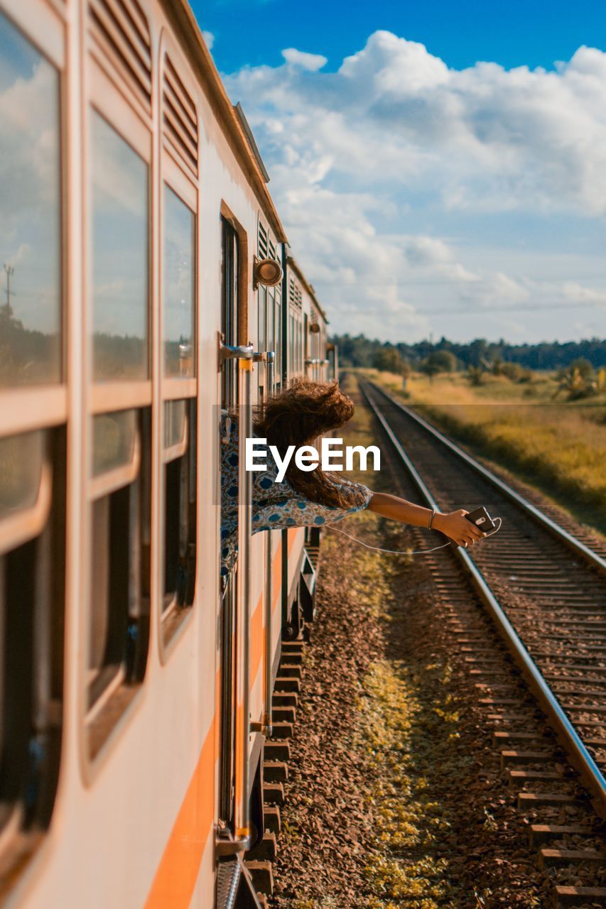 Rear view of happy woman holding mobile phone peeking through window while traveling in train