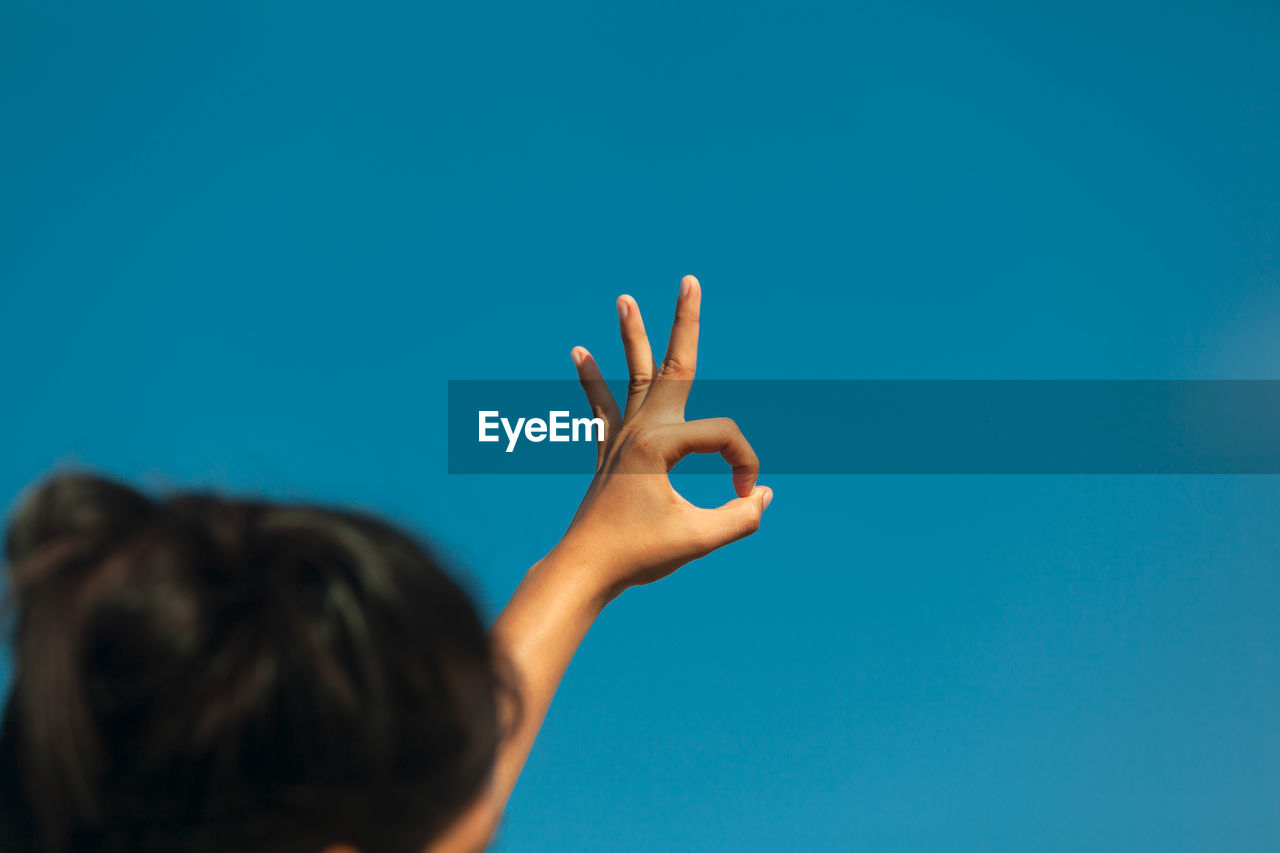 Woman gesturing against blue sky