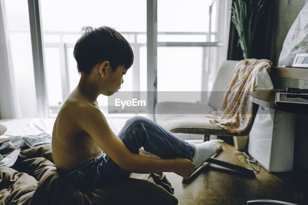 Shirtless boy wearing sock on bed at home